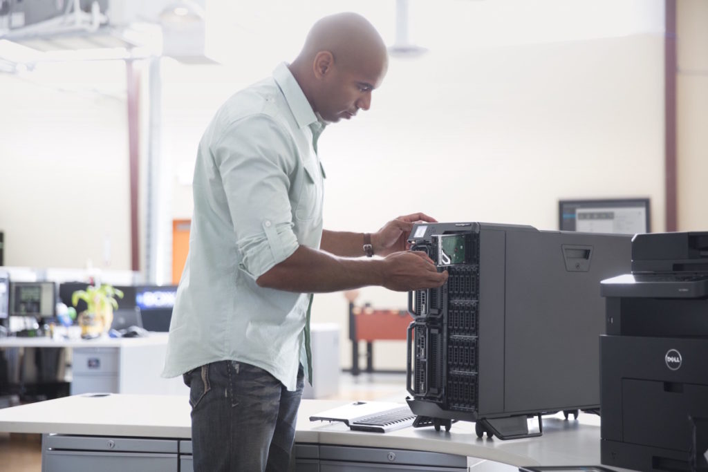 Man standing in front of a Dell PowerEdge VRTX server chassis populated with PowerEdge server products, adjusting a blade.