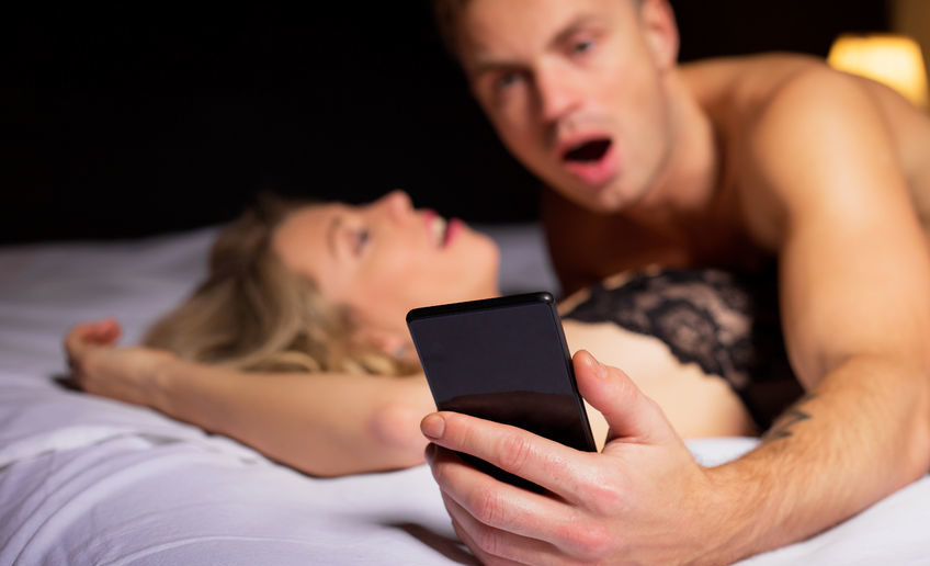 surprised man looking at his phone while laying on top of woman