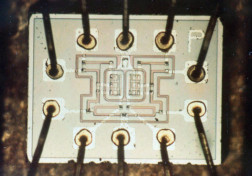 Raný integrovaný obvod v podobe logického hradla NOR od firmy Fairchild, zložený zo šiestich prepojených tranzistorov (štvorčeky v centre)