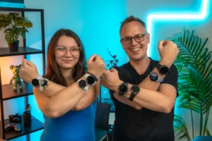 Dievča v modrom tričku a chlapec v modrom tričku s prekríženými oboma rukami, na ktorých majú množstvo rôznych smart hodiniek