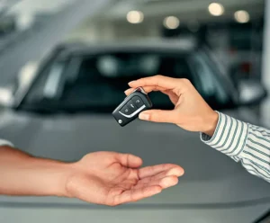 Dve ruky a jedna z nich drží kľúč od auta a v pozadí je rozmazané auto