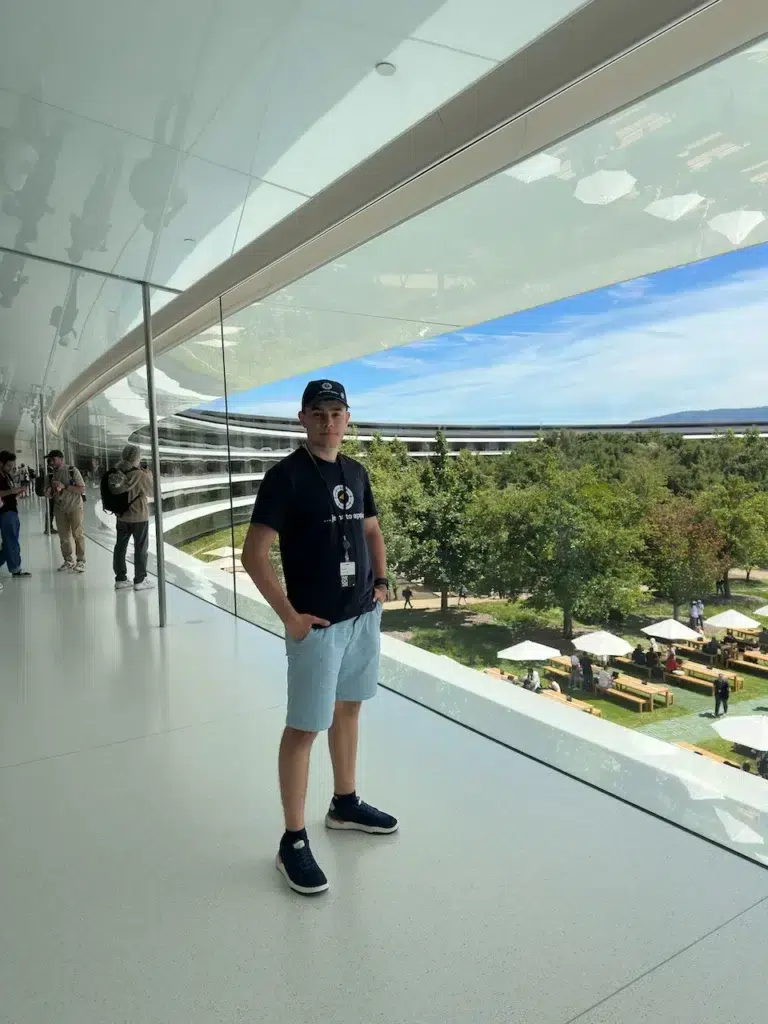 Záber zvnútra Apple Parku. Spoza zaoblenej presklenej steny vidno kruhovú budovu a vnútorné nádvorie so slnečníkmi